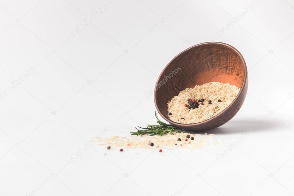raw rice and spices spilling out bowl on white surface