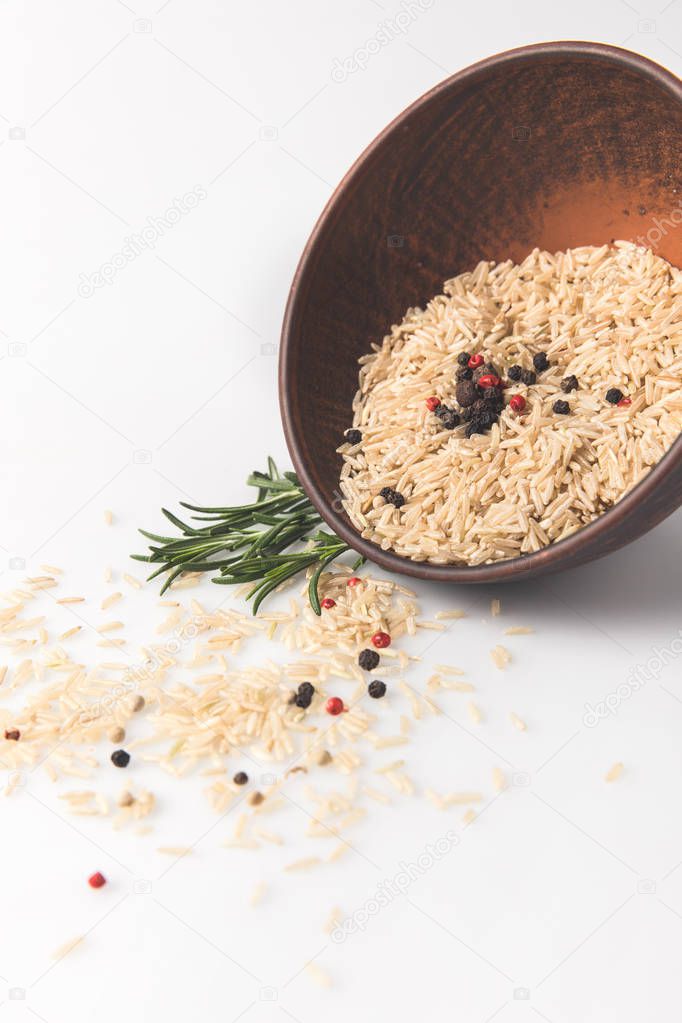 close-up shot of raw rice and spices spilling out bowl on white surface