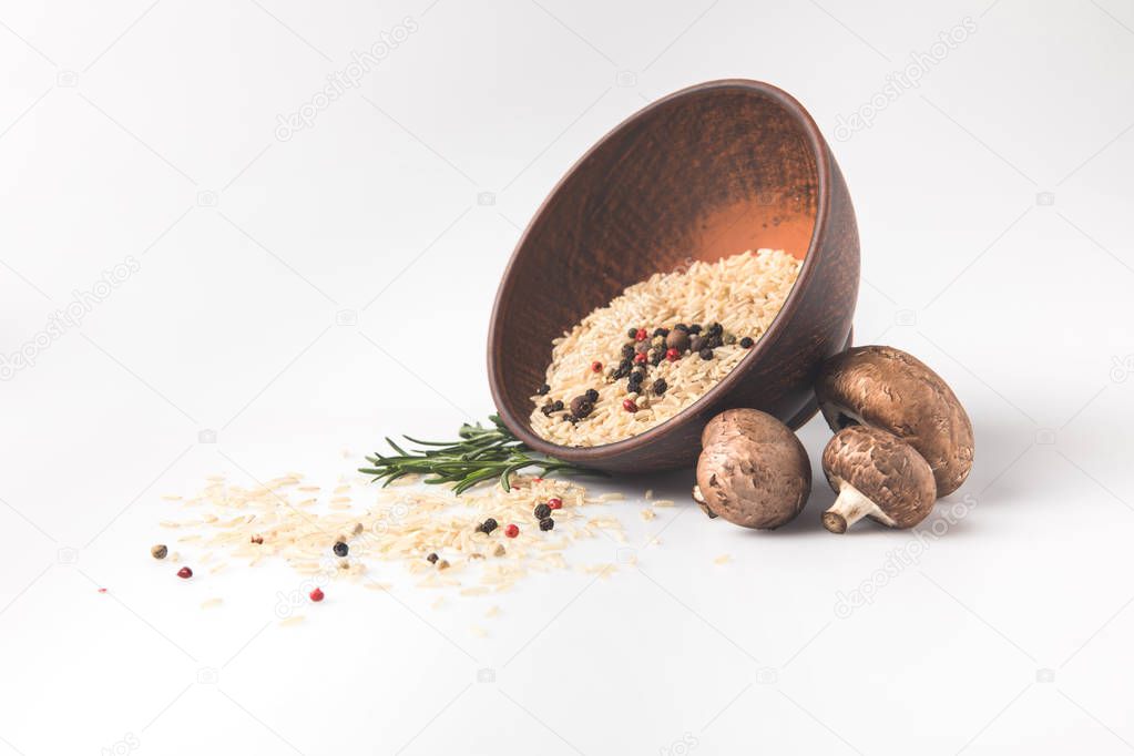 raw rice spilling out bowl on white surface with mushrooms