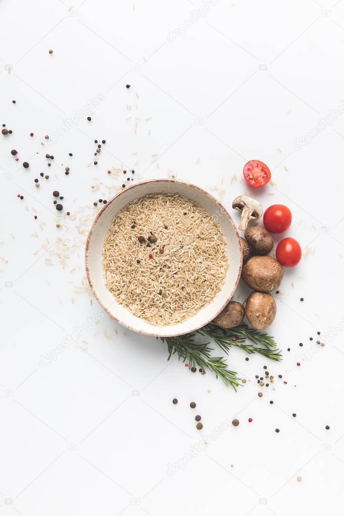 flat lay composition of raw rice in bowl with mushrooms and tomatoes on white surface