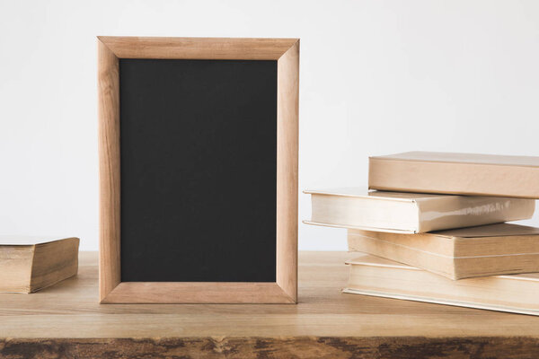 stack of old books and blackboard in frame on wooden table on white 