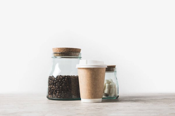 coffee beans, refined sugar and disposable coffee cup on marble table on white 