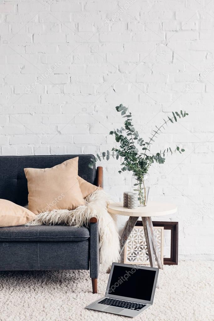 laptop on floor of white living room interior with cozy couch, mockup concept