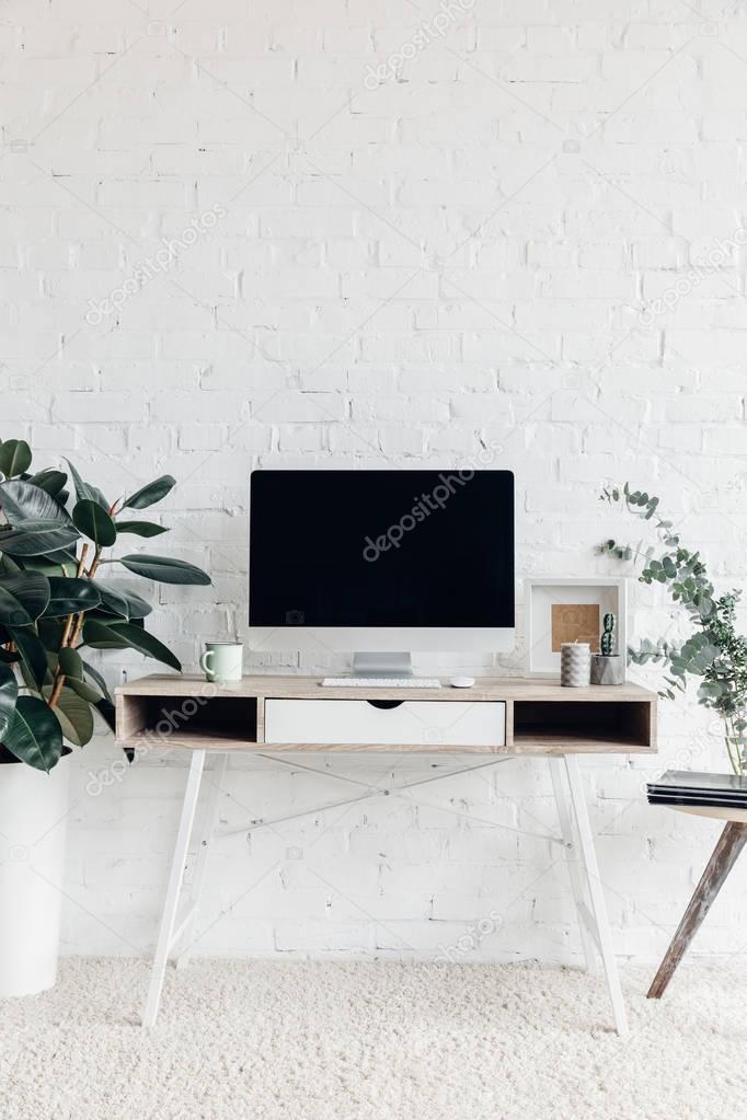 blank copmuter screen on workplace surrounded with flower pots, mockup concept