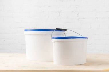 two plastic buckets with paints on wooden surface clipart