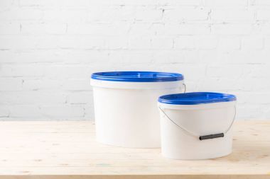 two plastic buckets with paints on wooden table clipart