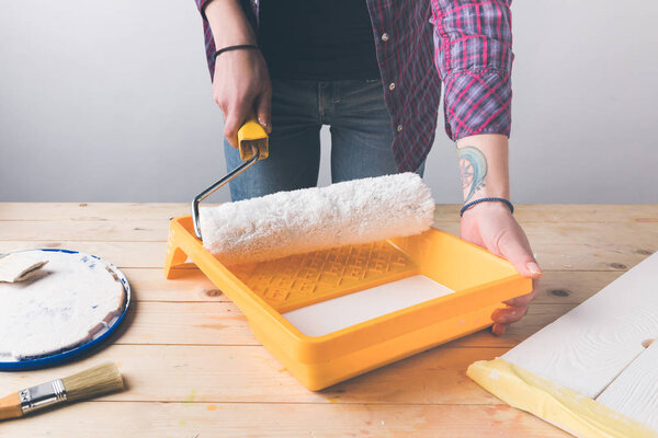 cropped image of woman holding paint roll brush above tray with paint