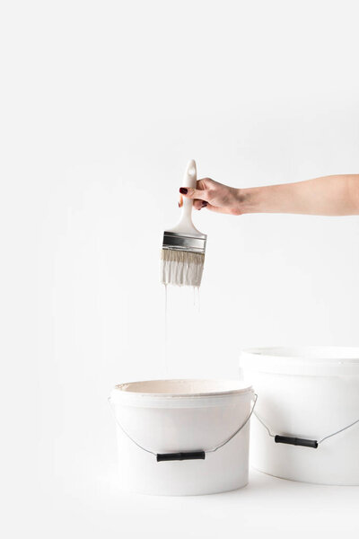 cropped image of girl holding brush in white paint above buckets isolated on white