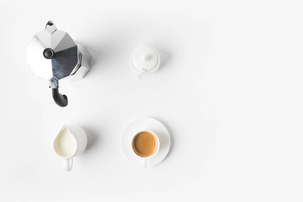 top view of arranged cup of coffee, jag of milk and coffee maker on white surface 