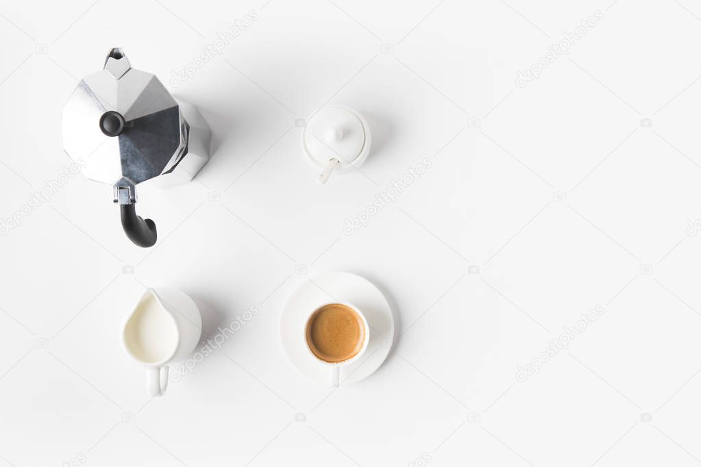 top view of arranged cup of coffee, jag of milk and coffee maker on white surface 