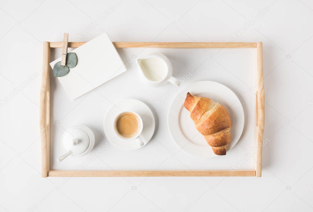 flat lay with cup coffee and croissant for breakfast on tray on white tabletop