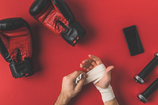 обрезанный снимок боксера, закрывающего руки эластичной повязкой на красной поверхности
