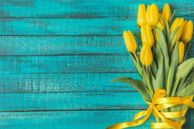 beautiful yellow tulips with ribbon on turquoise wooden surface 