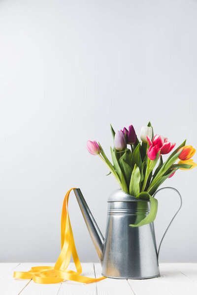 beautiful colorful tulips in watering can with yellow ribbon on grey  