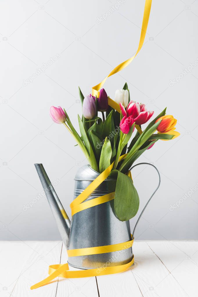beautiful blooming tulip flowers in watering can with yellow ribbon on grey
