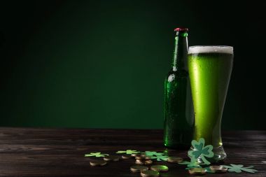 glass bottle and glass of green beer with coins on wooden table, st patricks day concept clipart