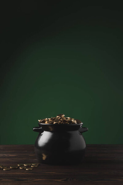 black pot of golden coins on wooden table on green, st patricks day concept