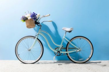 side view of bicycle with flowers in basket in front of blue wall clipart