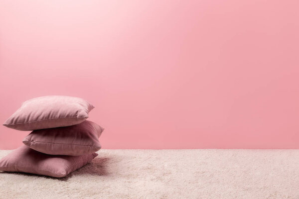 stack of pillows on carpet in front of pink wall