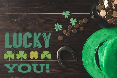 flat lay with horseshoe, hat and pot of gold on wooden tabletop with lucky you lettering clipart