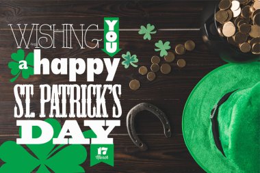 flat lay with horseshoe, hat and pot of gold on wooden tabletop with wishing you a happy st patricks day lettering clipart