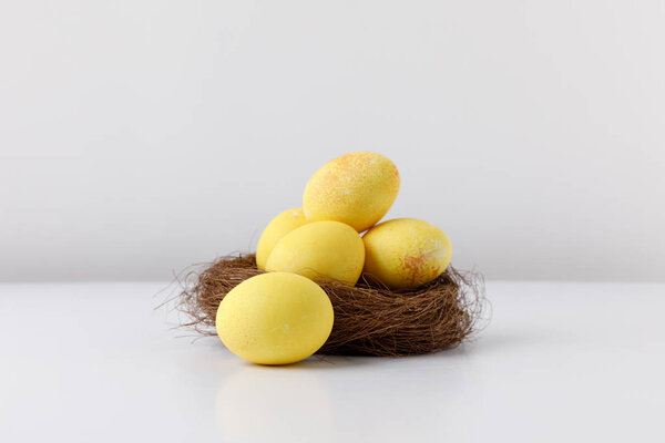 желтые окрашенные пасхальные яйца в декоративное гнездо на белом столе
