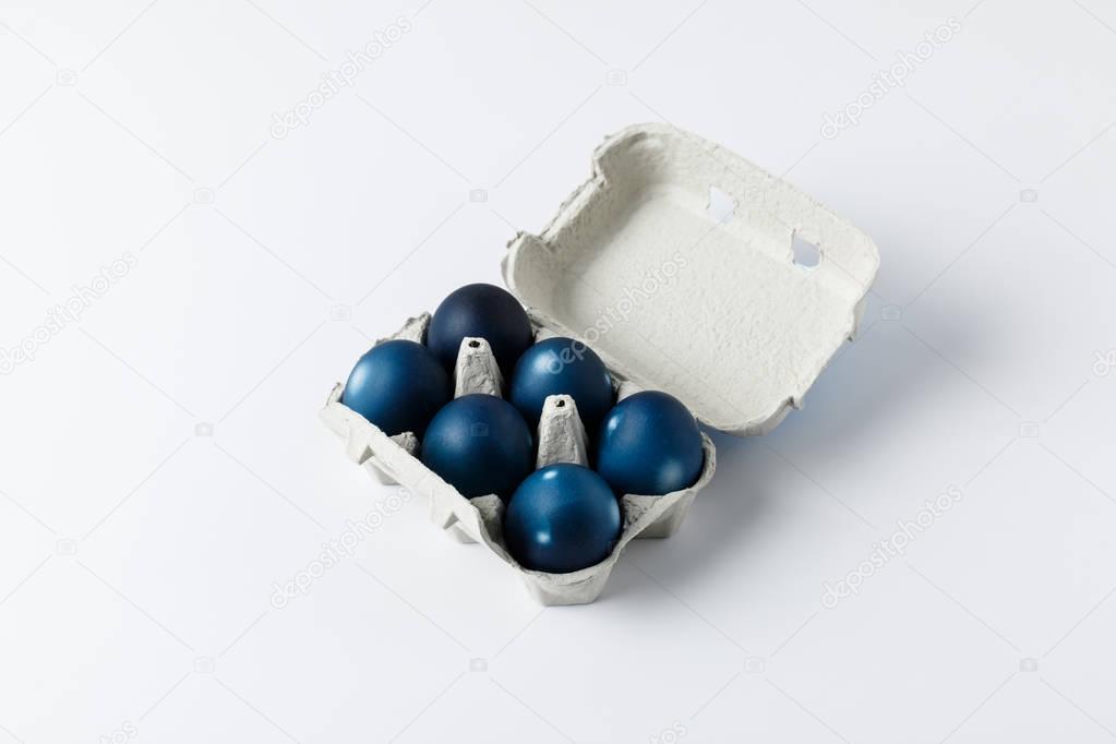 six blue painted easter eggs in egg tray on white
