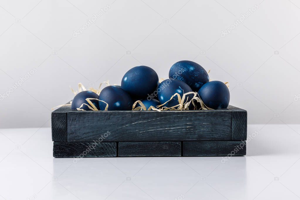 blue painted easter eggs in box with decorative hay on white