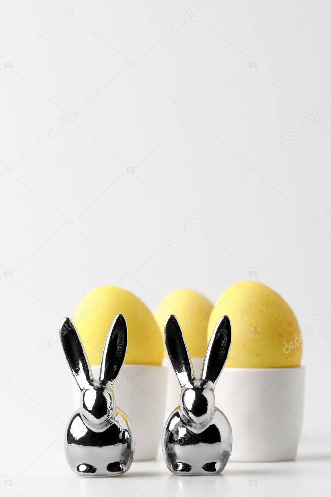 yellow painted easter eggs in egg stands and statuettes of rabbits on white