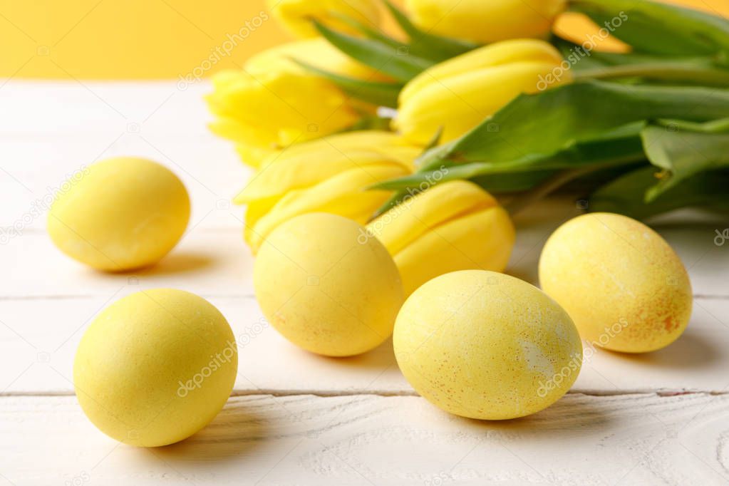 yellow painted easter eggs with tulips on wooden table