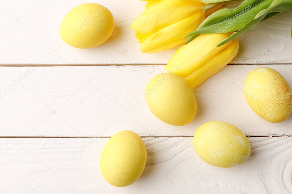 top view of yellow painted easter eggs with tulips on wooden table