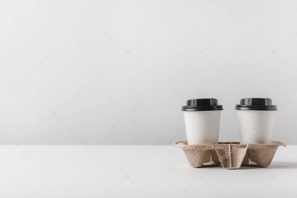 two coffee in paper cups in cardboard tray on table