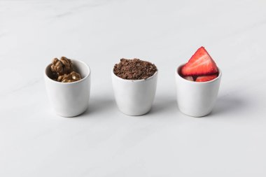 Closeup view of three bowls with walnuts, grated chocolate and strawberries on gray clipart