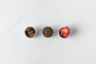Three bowls with walnuts, grated chocolate and strawberries on white clipart