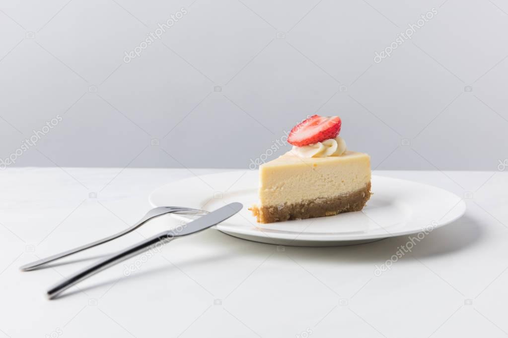 Cheesecake with piece of fresh strawberry on white plate and cutlery