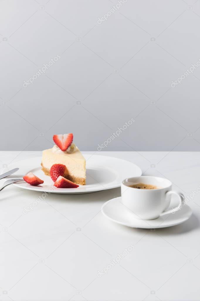 Coffee cup and cutlery near plate with strawberry cheesecake