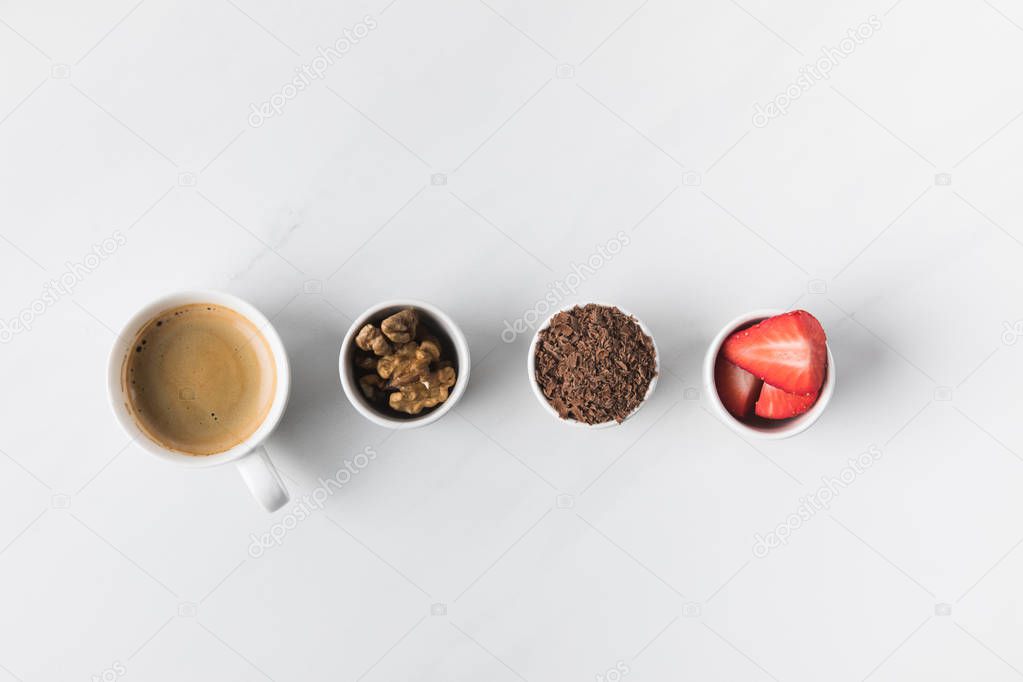 Top view of coffee cup and bowls with walnuts, strawberries and grated chocolate