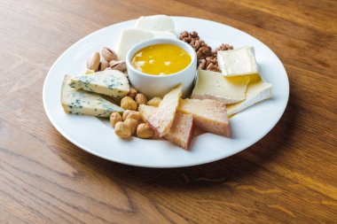close-up view of delicious cheese plate with nuts and honey on wooden tabletop clipart