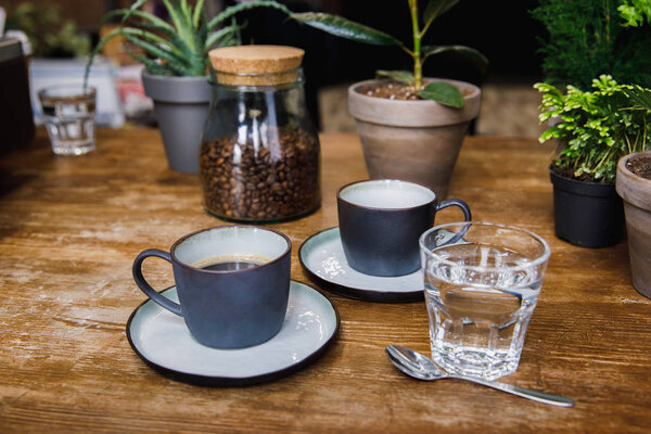 Cups of coffee and glass of water on table in cozy coffee shop
