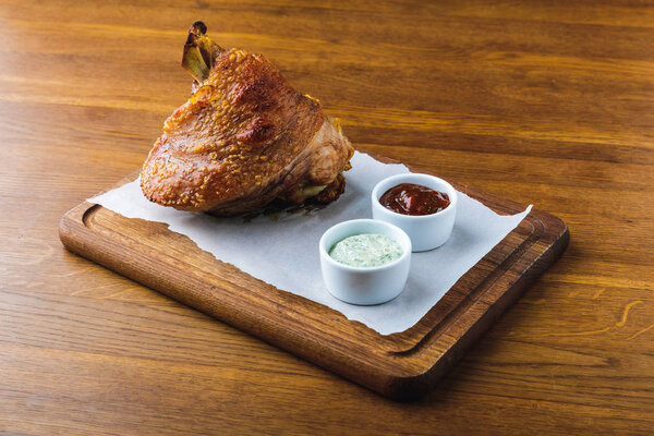 close-up view of gourmet roasted pork knuckle with sauces on wooden tabletop