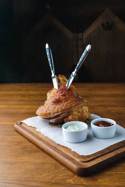 roasted pork knuckle with knives and sauces on wooden tabletop