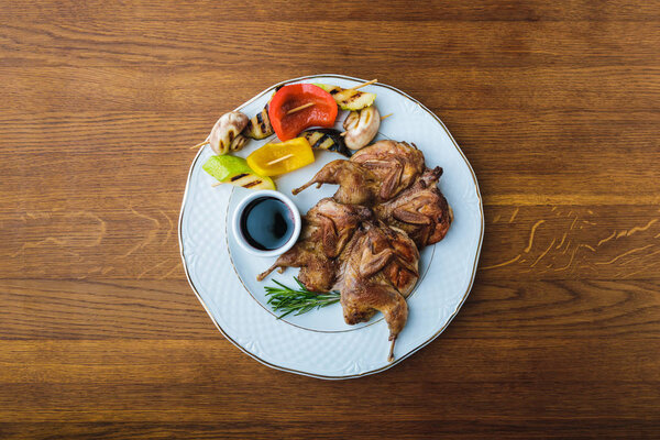top view of roasted chickens with grilled vegetables and sauce on plate