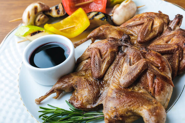 close-up view of roasted chickens with grilled vegetables and sauce on plate