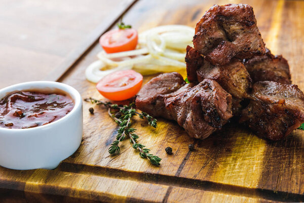 delicious grilled meat with vegetables and bbq sauce on wooden board  