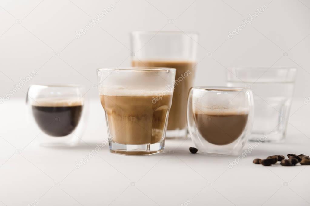 Glasses with assorted coffee drinks on white background with coffee beans
