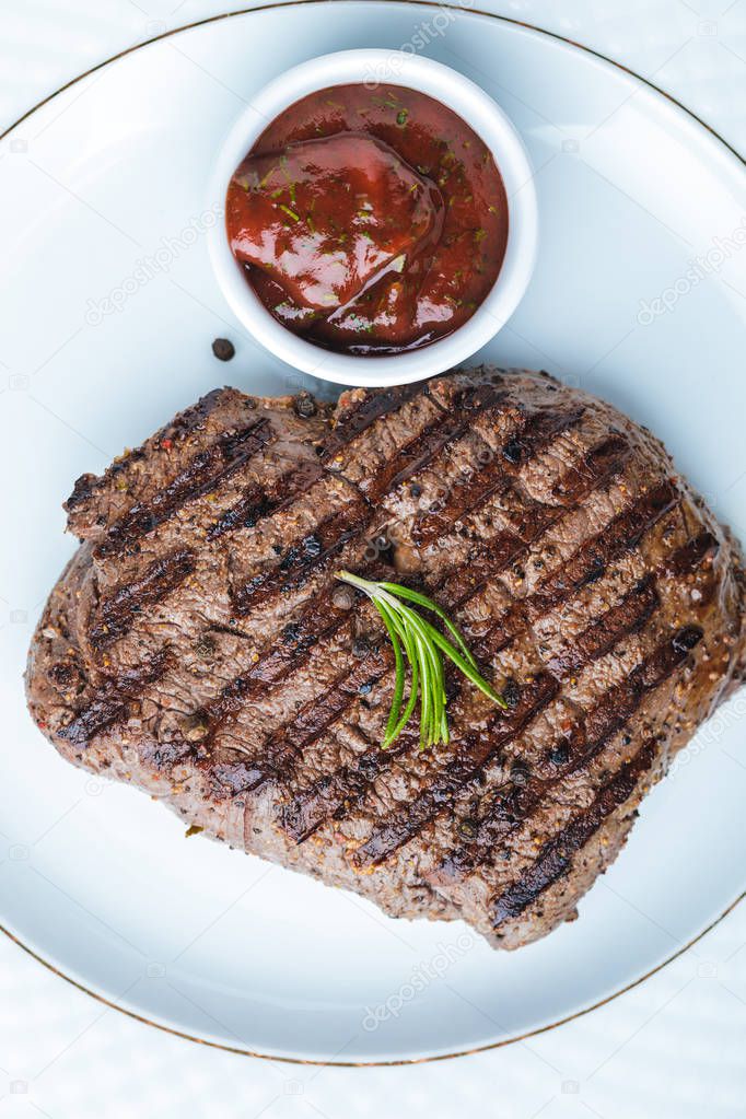 top view of tasty grilled steak with rosemary and bbq sauce on plate