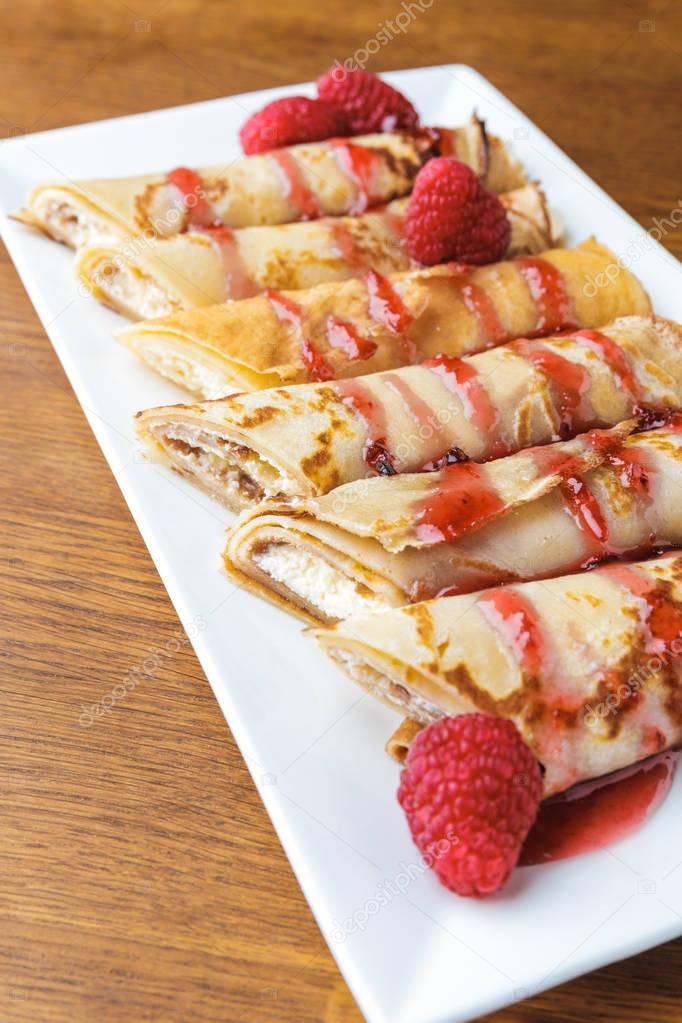 close-up view of delicious sweet rolled pancakes with raspberries and jam 