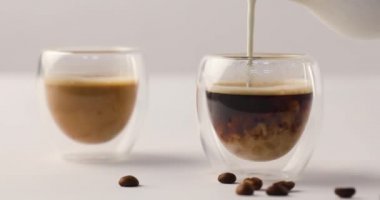 Birinde iki bardak kahve kahve çekirdekleri ters görüntüleri ile beyaz zemin üzerine dökülen süt