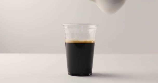 把牛奶从壶里倒在塑料杯里 用咖啡在白色背景上与背面的镜头 — 图库视频影像