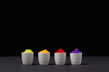 row of colorful holi paint in four bowls on black, Hindu spring festival clipart